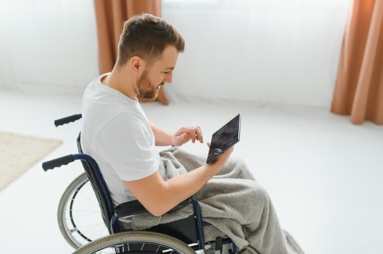 Man in wheelchair using tablet computer at home. Positive retired male with physical disability