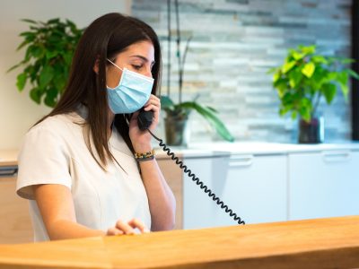 receptionist-wearing-a-face-mask-takes-a-call-while-working-at-a-reception-desk.jpg